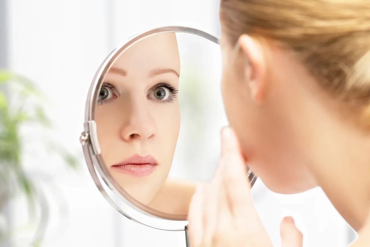 a woman looking at her face in a mirror
