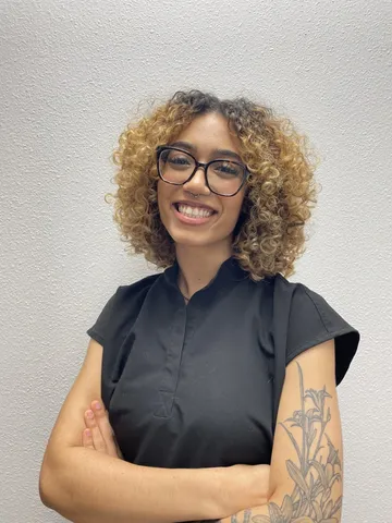 a woman with curly hair wearing glasses and a tattoo on her arm - taryn